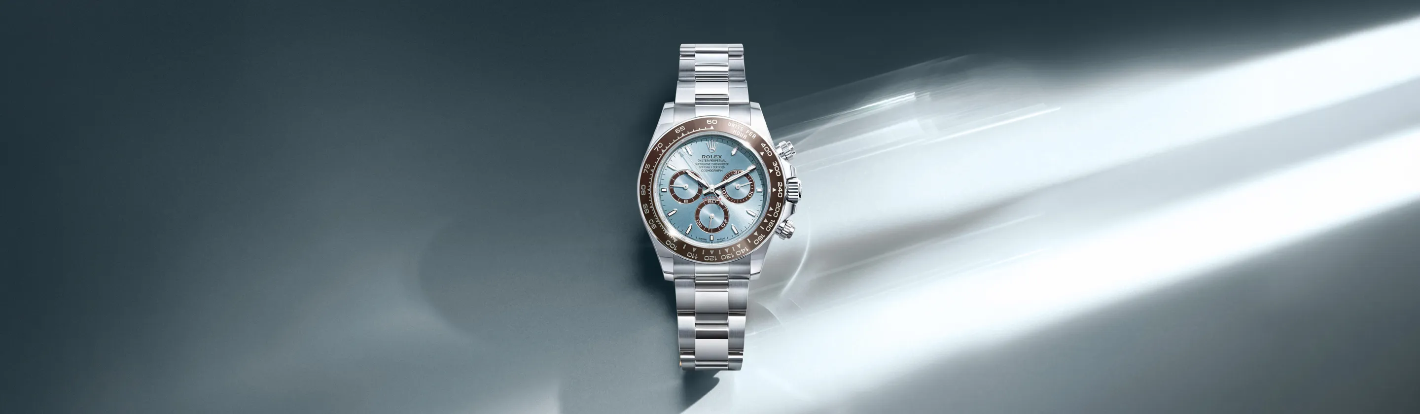 rolex-cosmograph-daytona-cover-m126506-0001-landscape Stainless steel Rolex wristwatch with a light blue dial and brown bezel, laid on a reflective, gradient background.