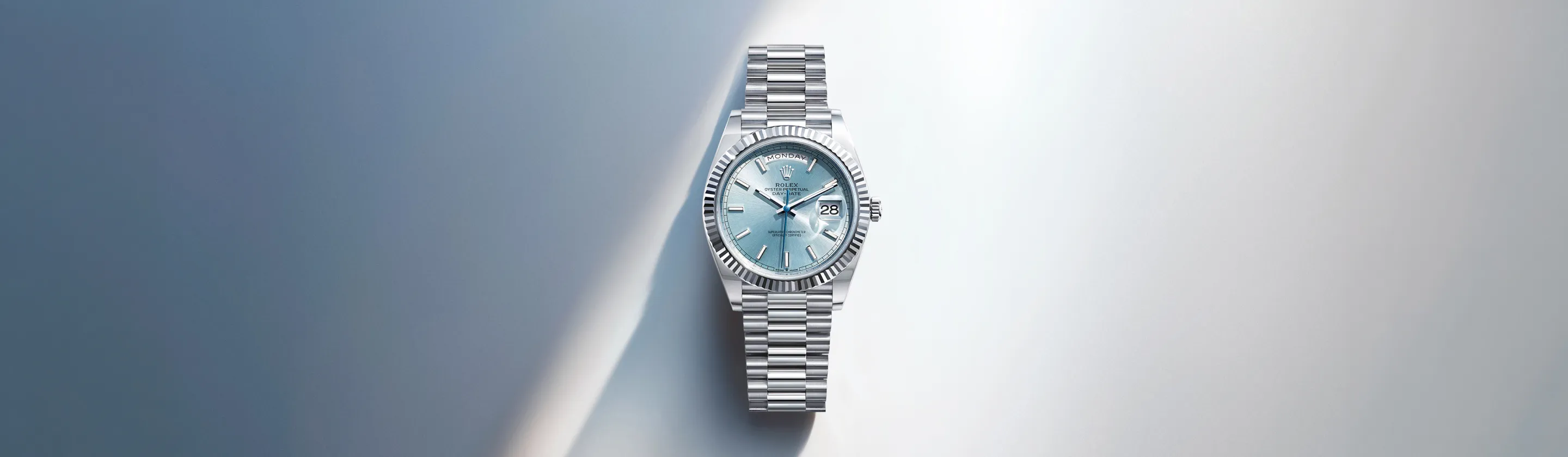 rolex-day-date-cover-m128236-0018-landscape Silver Rolex Day-Date watch with a light blue dial, date window, and fluted bezel on a blue gradient background.