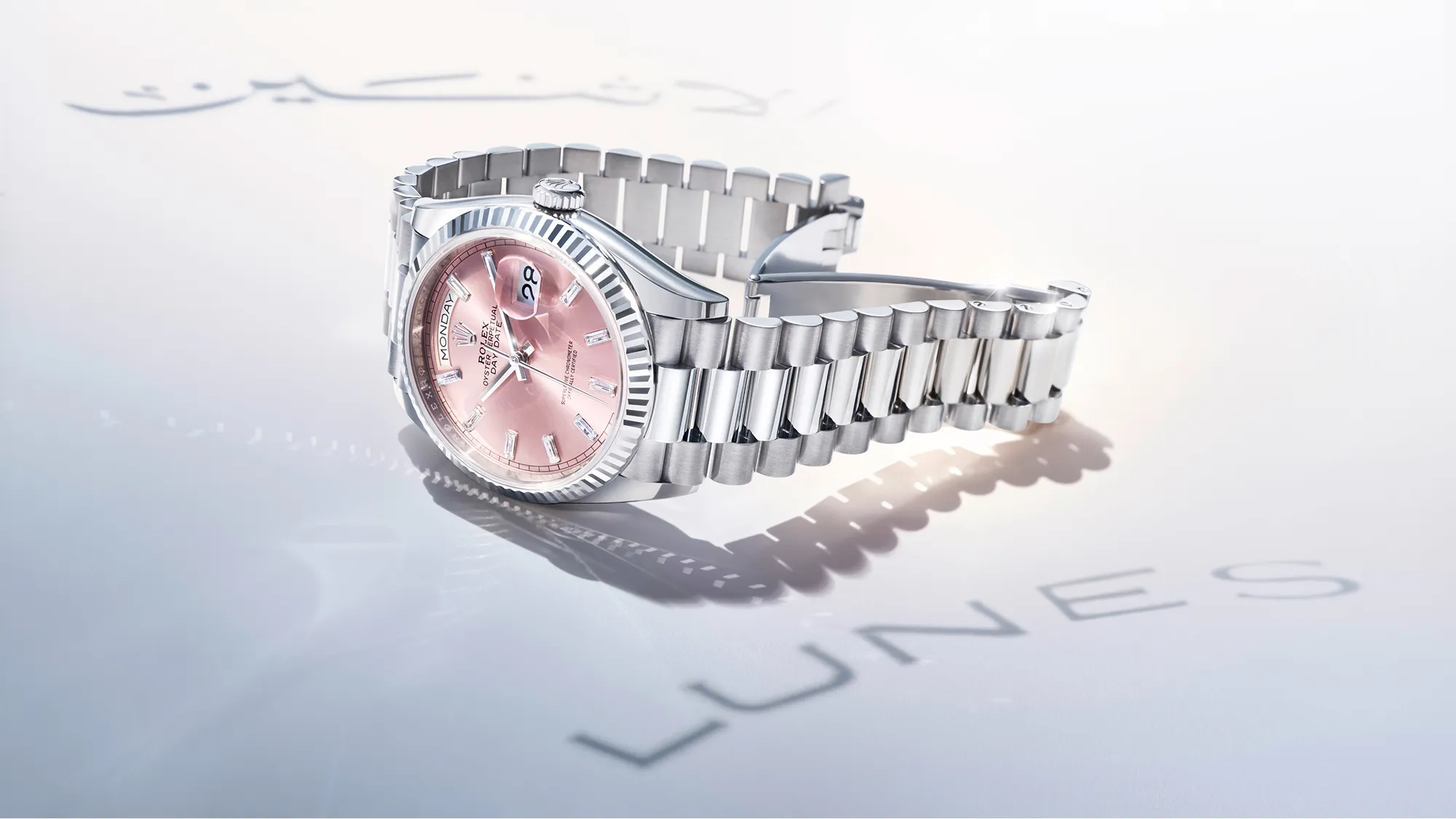 rolex-day-date-m128239-0071-landscape Rolex stainless steel watch with a pink dial and date window resting on a glossy surface.
