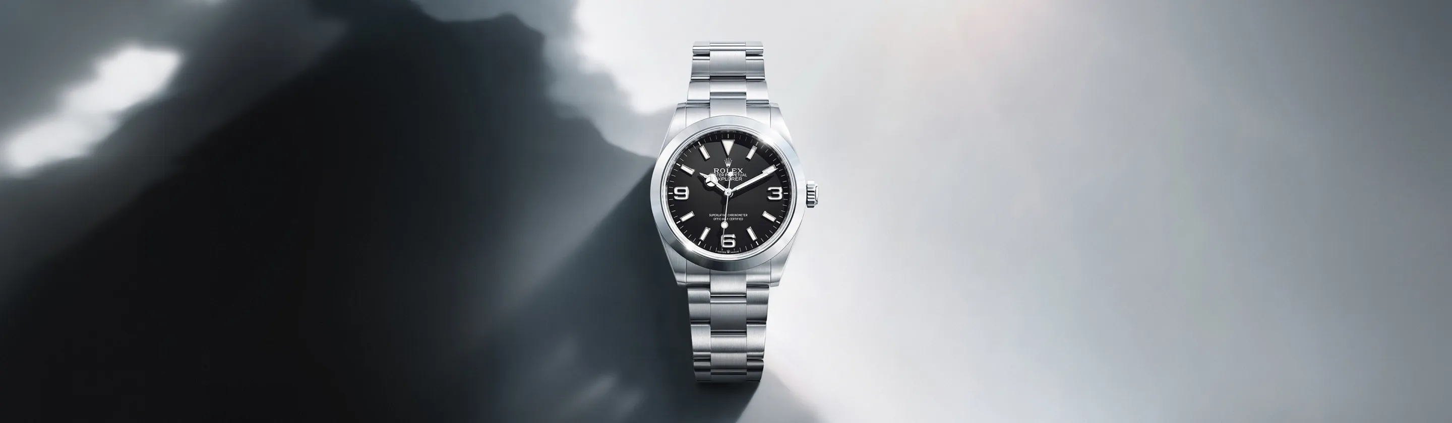 rolex-explorer-cover-m224270-0001-landscape Silver Rolex stainless steel wristwatch with a black dial against a gray gradient background.