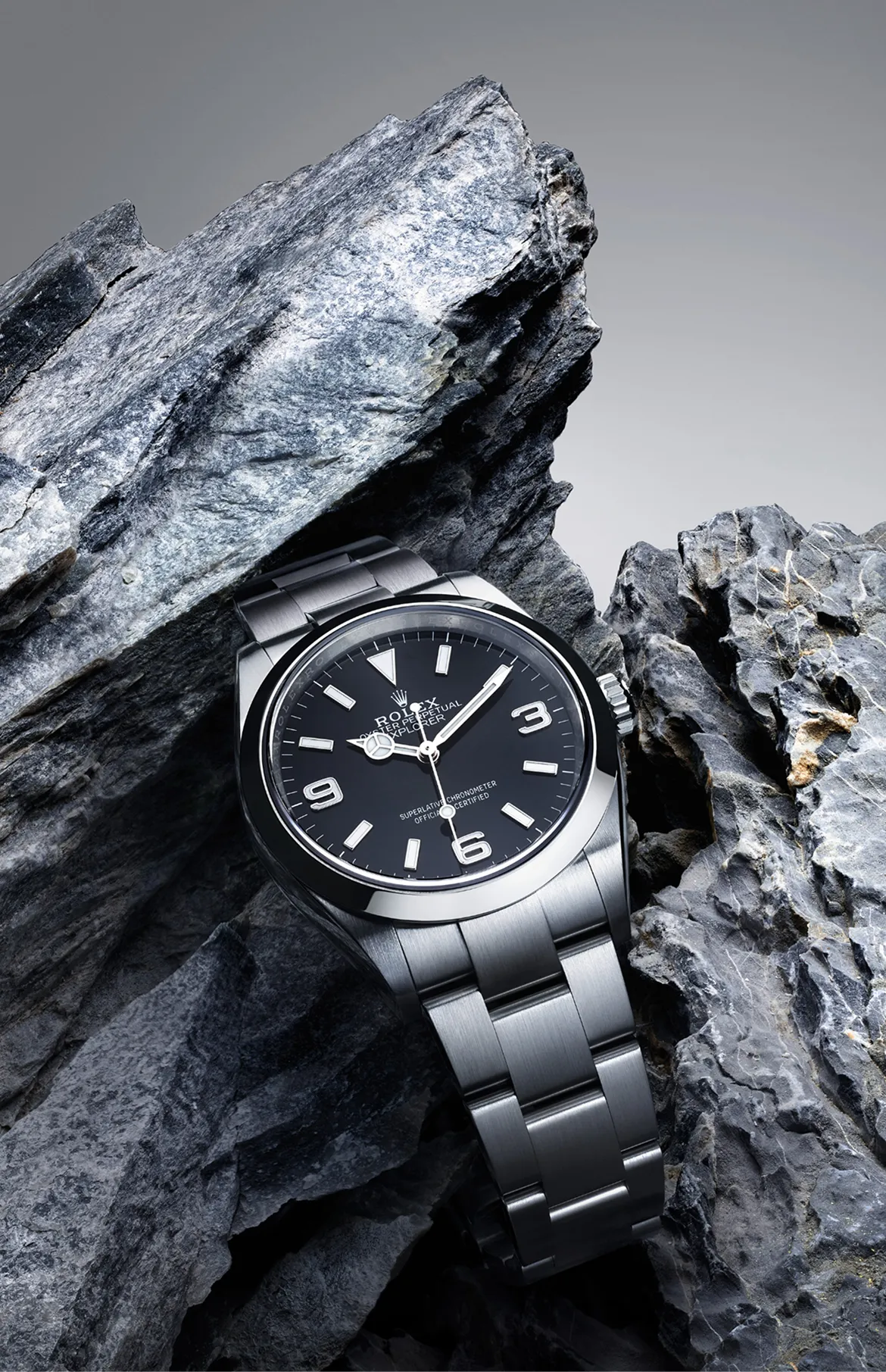 rolex-explorer-exceptional-chronometric-precision-m124270-0001-portrait Stainless steel Rolex Explorer watch wedged among rugged rocks, close-up of black dial with white numerals 3, 6 and 9.