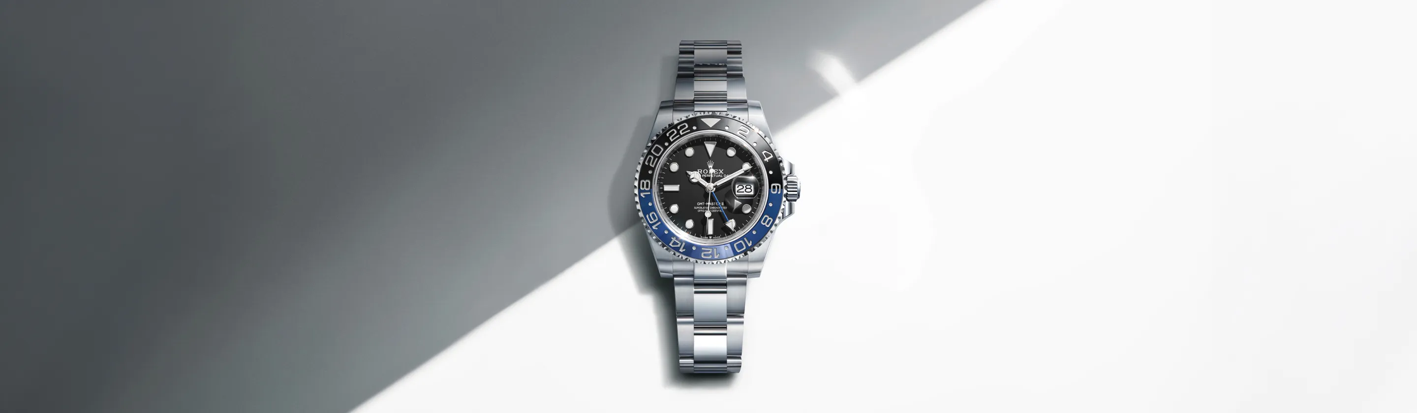 rolex-gmt-master-ii-cover-m126710blnr-0003-landscape Rolex GMT-Master II stainless steel watch with a black dial and blue-and-black bezel on a diagonal gray-white background.