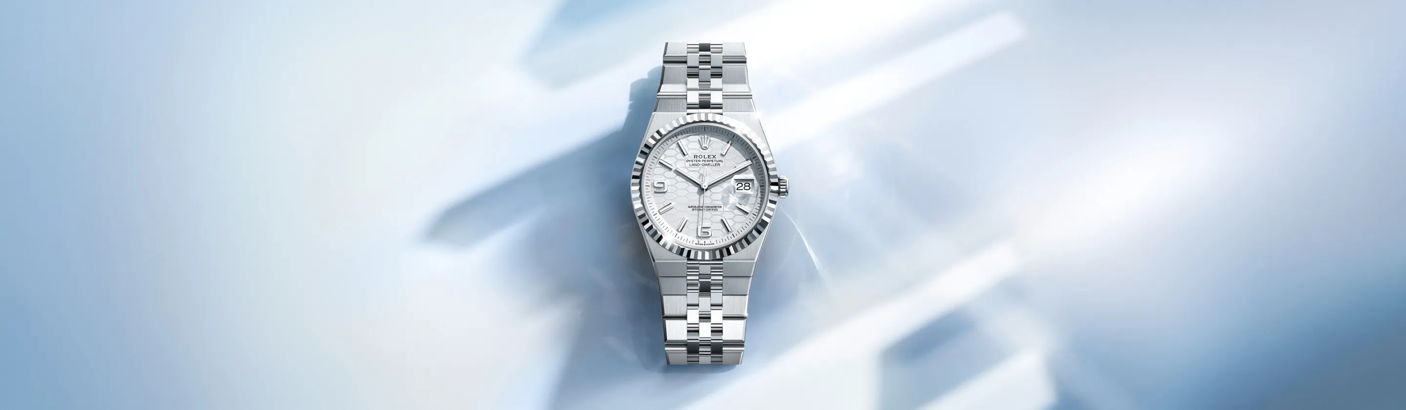 Stainless steel Rolex wristwatch with a silver dial and date window, shown on a pale blue background.