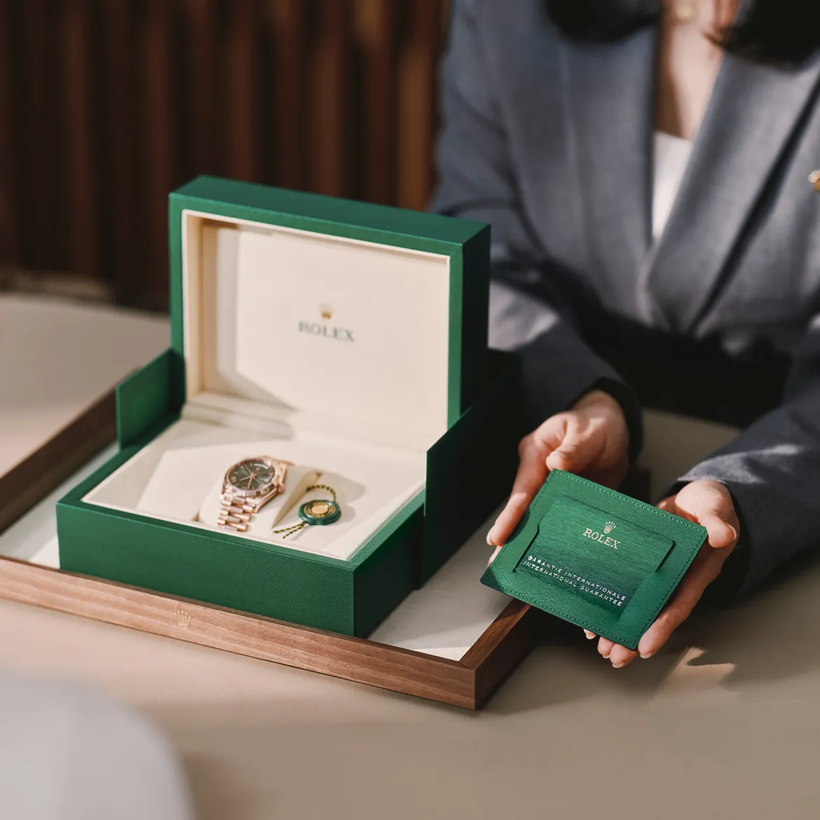 rolex-our-rolex-services-portrait | Brela Open green Rolex box reveals a gold Rolex watch with bracelet inside; a person holds a green warranty card nearby. | Brela