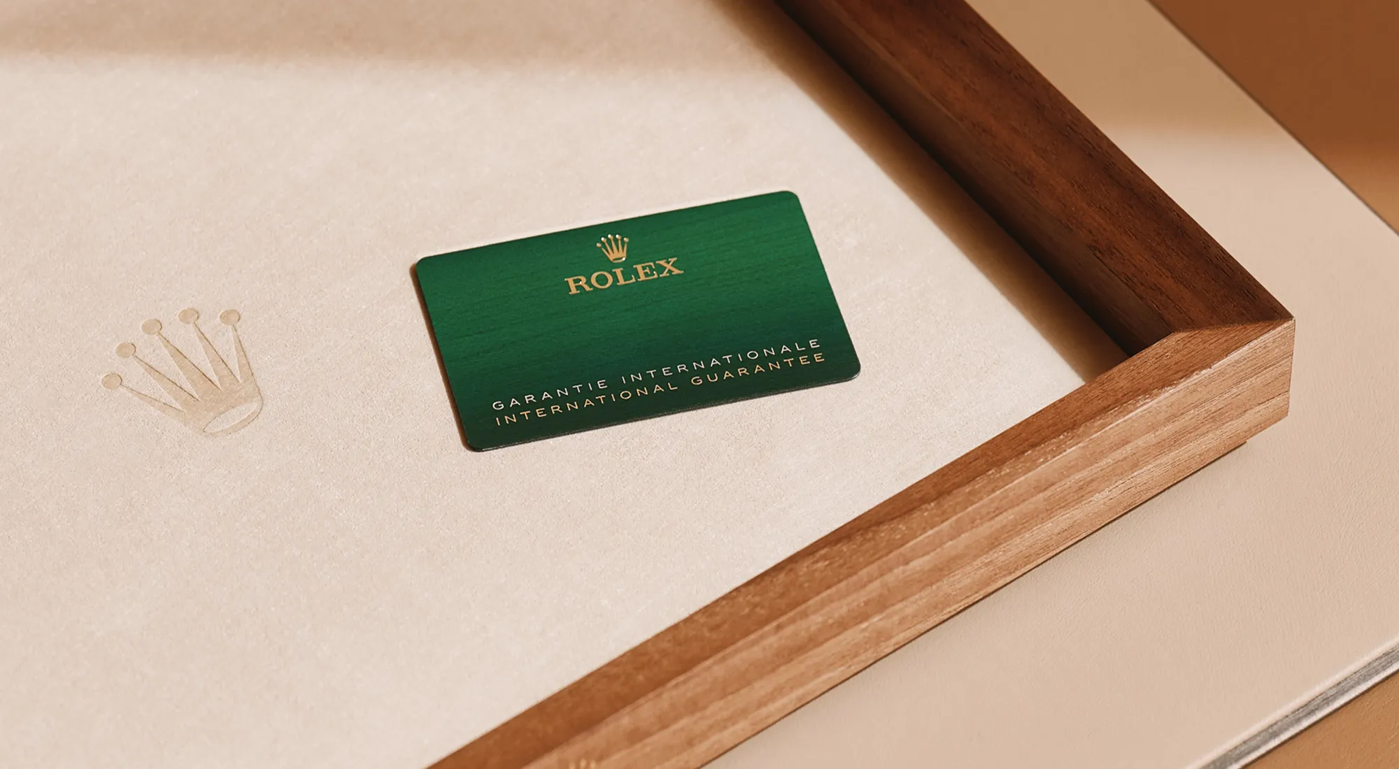 rolex-servicing-elmt_2603fg_011-landscape | Brela Green Rolex warranty card resting on beige fabric inside an open wooden box, with gold lettering and crown logo visible. | Brela