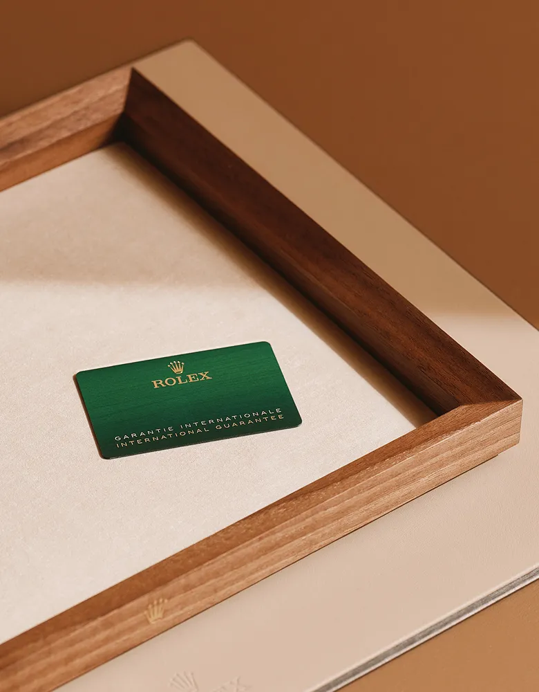 rolex-servicing-elmt_2603fg_011-portrait | Brela Green Rolex warranty card resting in a light wood display tray on a beige surface. | Brela