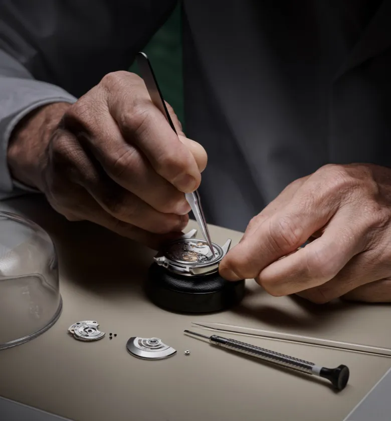 rolex-servicing-sav_1910dh_005-portrait | Brela Close-up of hands using tweezers to assemble a mechanical watch, with tiny parts on a workbench | Brela
