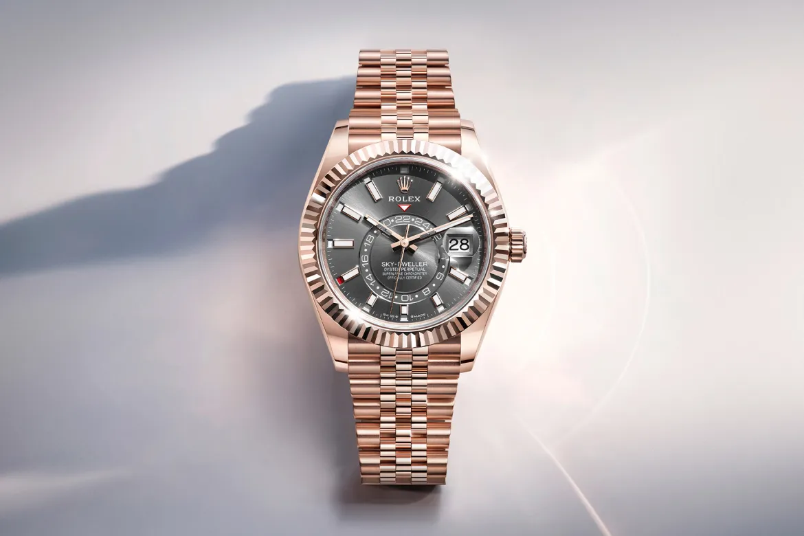 Rose gold Rolex Sky-Dweller watch with a grey dial, fluted bezel, and date window at 3 o'clock on a pale surface.