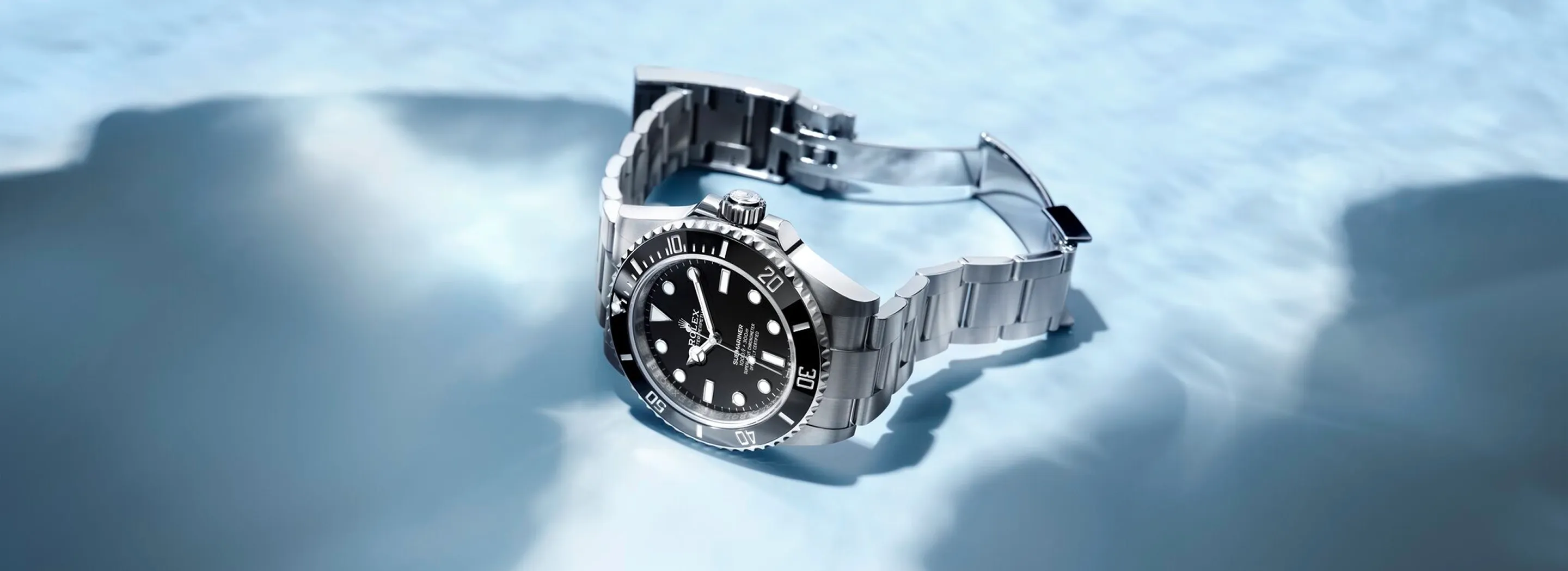 Silver stainless steel wristwatch with a black dial resting on a blue, reflective water-like surface.