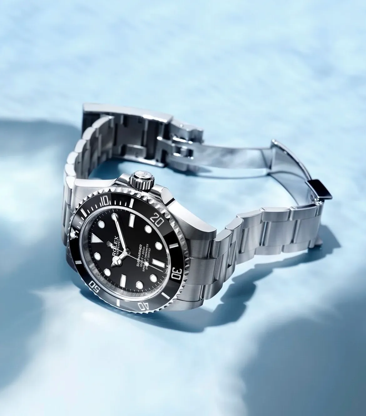 Stainless steel Rolex dive watch with black dial and rotating bezel on a blue surface.