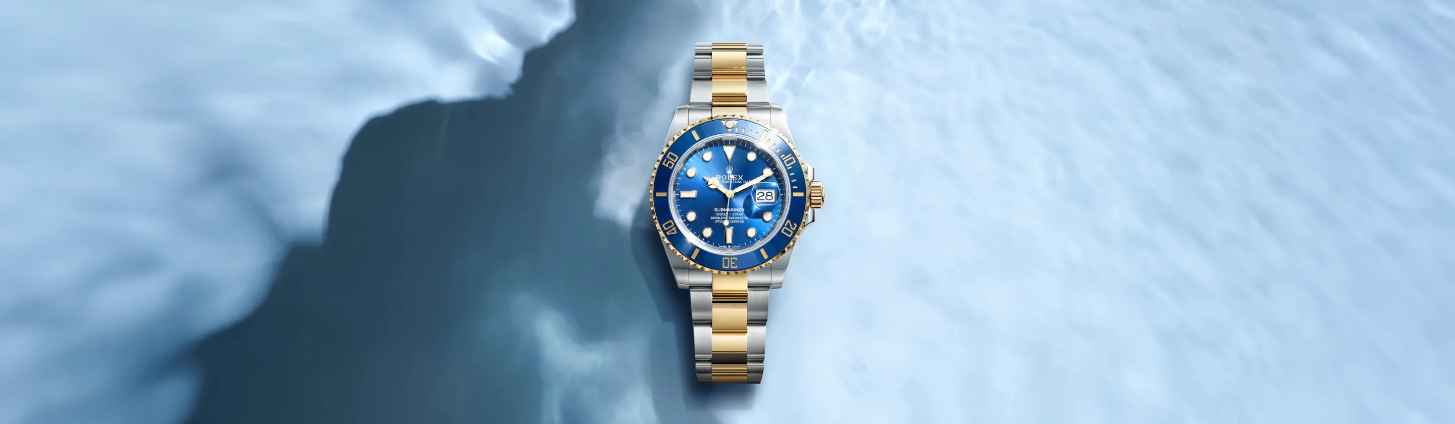 Two-tone Rolex Submariner watch with blue dial and date window, centered on a pale blue backdrop.