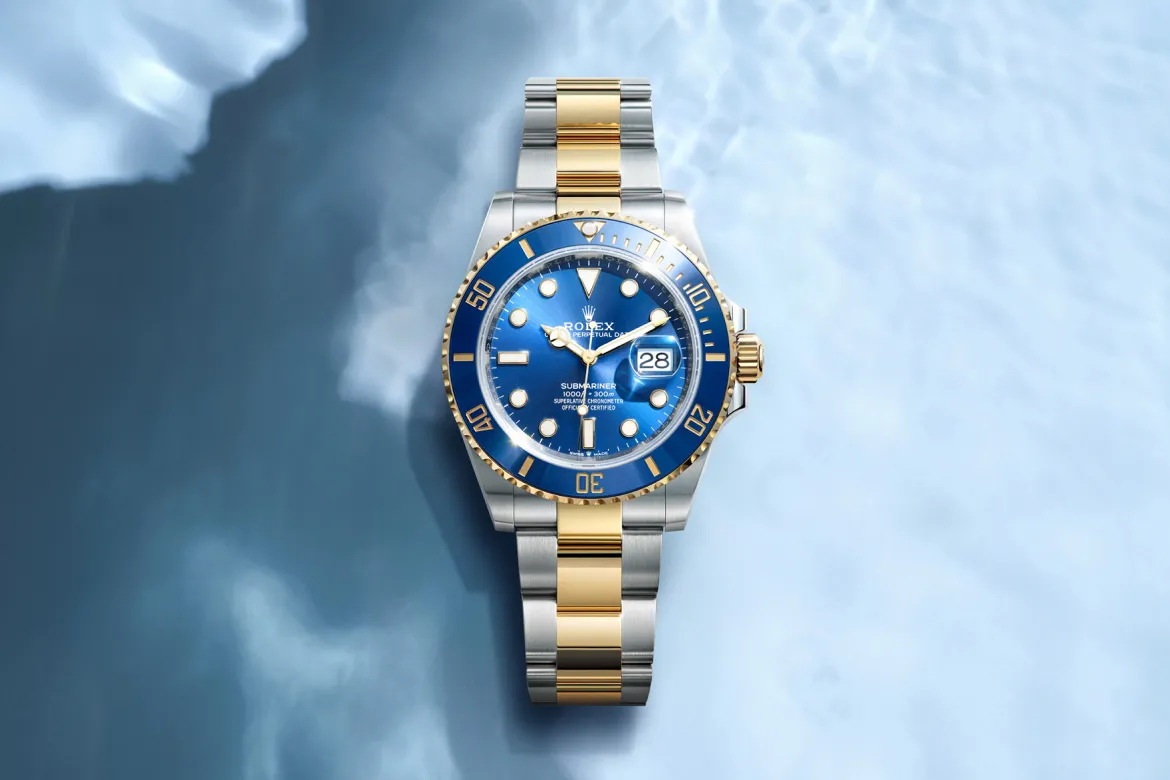 Two-tone Rolex Submariner with blue dial and date display on a silver‑and‑gold bracelet against a blue cloudy background