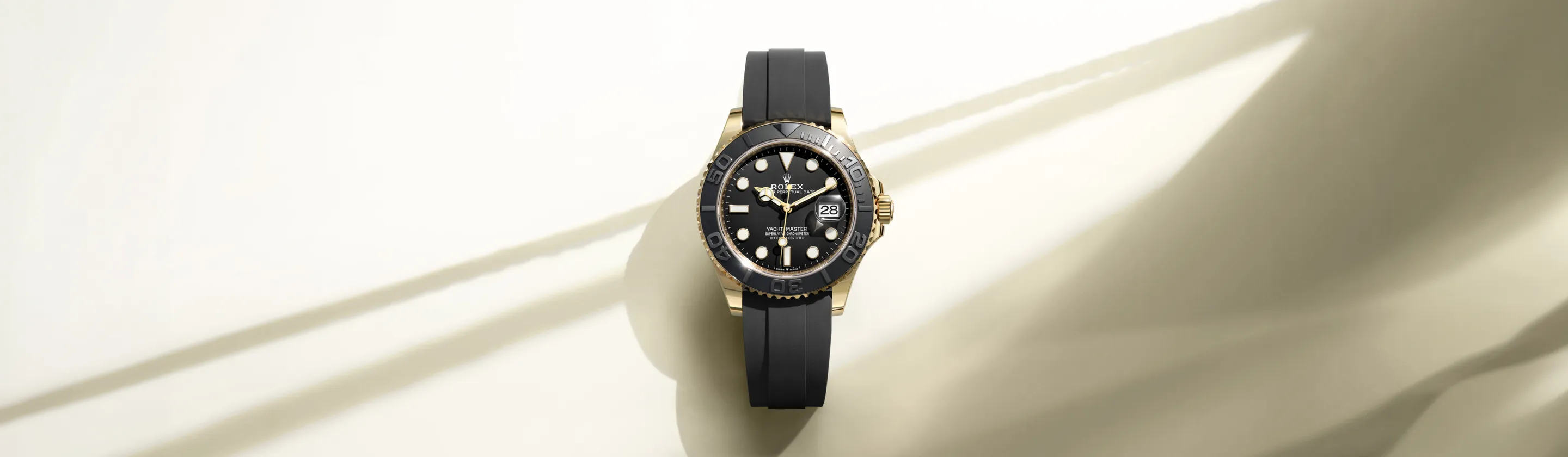 rolex-yacht-master-cover-m226658-0001-landscape Gold Rolex Yacht-Master watch with black dial and black rubber strap on a pale background.