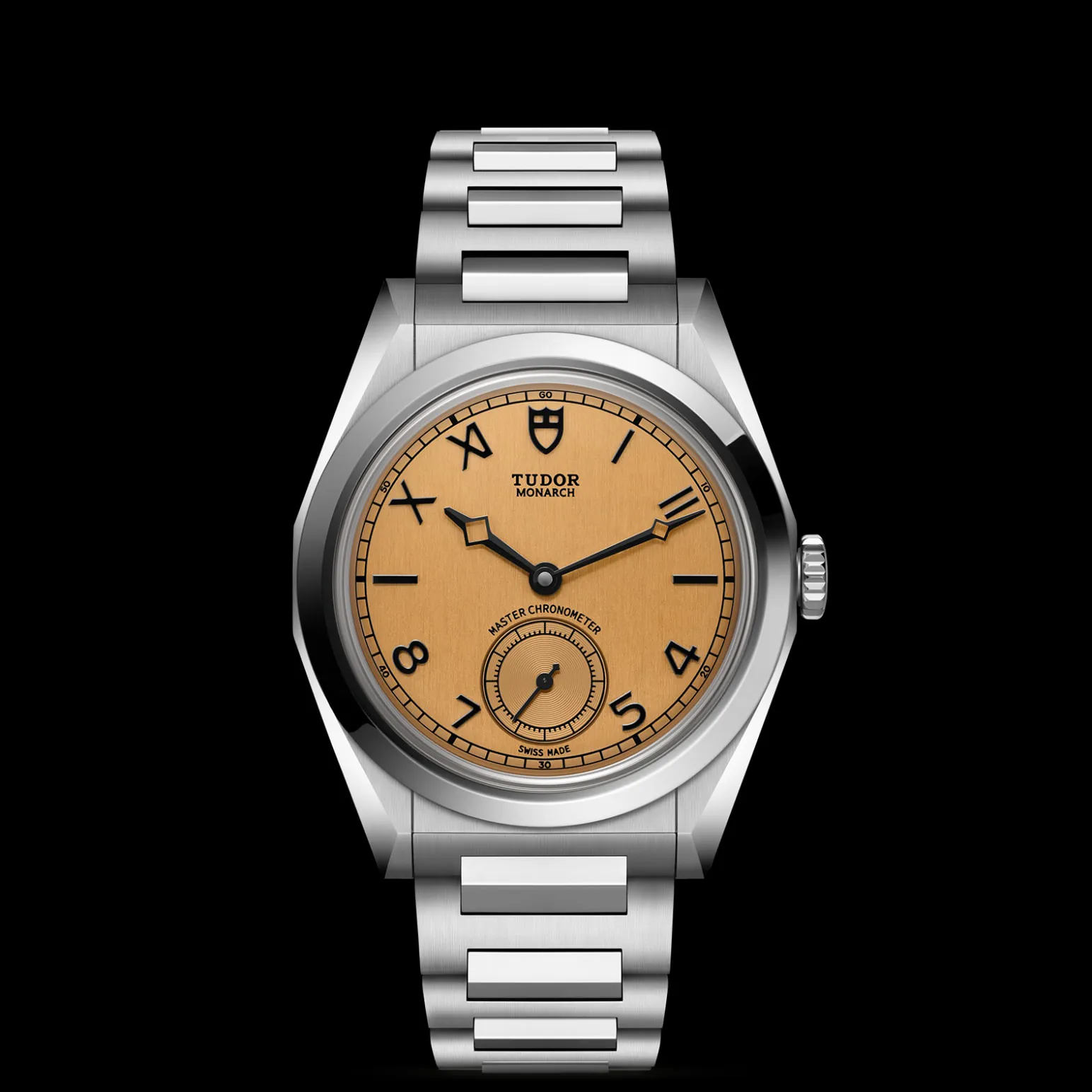 m2639w1a0u-0001-upright_watch_black_background_zoomed_in | Brela Stainless steel Tudor Monarch wristwatch with a gold dial, black hands, and a linked bracelet on a black background; close-up view of the face and crown. | Brela