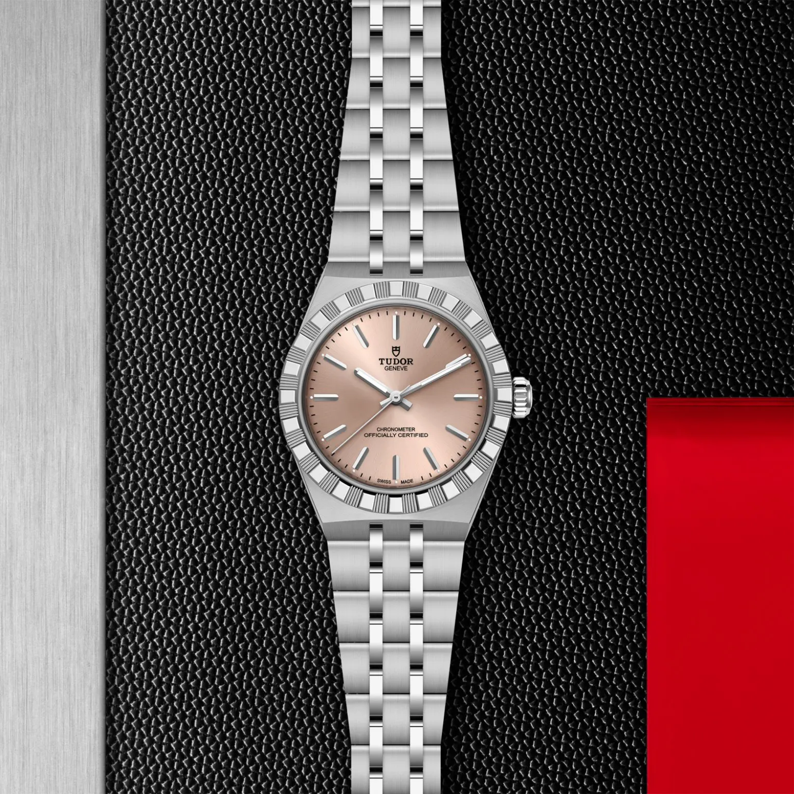 m2830a1a0-0003in_store_flat_lay | Brela Tudor stainless steel wristwatch with a pink dial and brushed bracelet set against a textured black background with a red panel on the right. | Brela