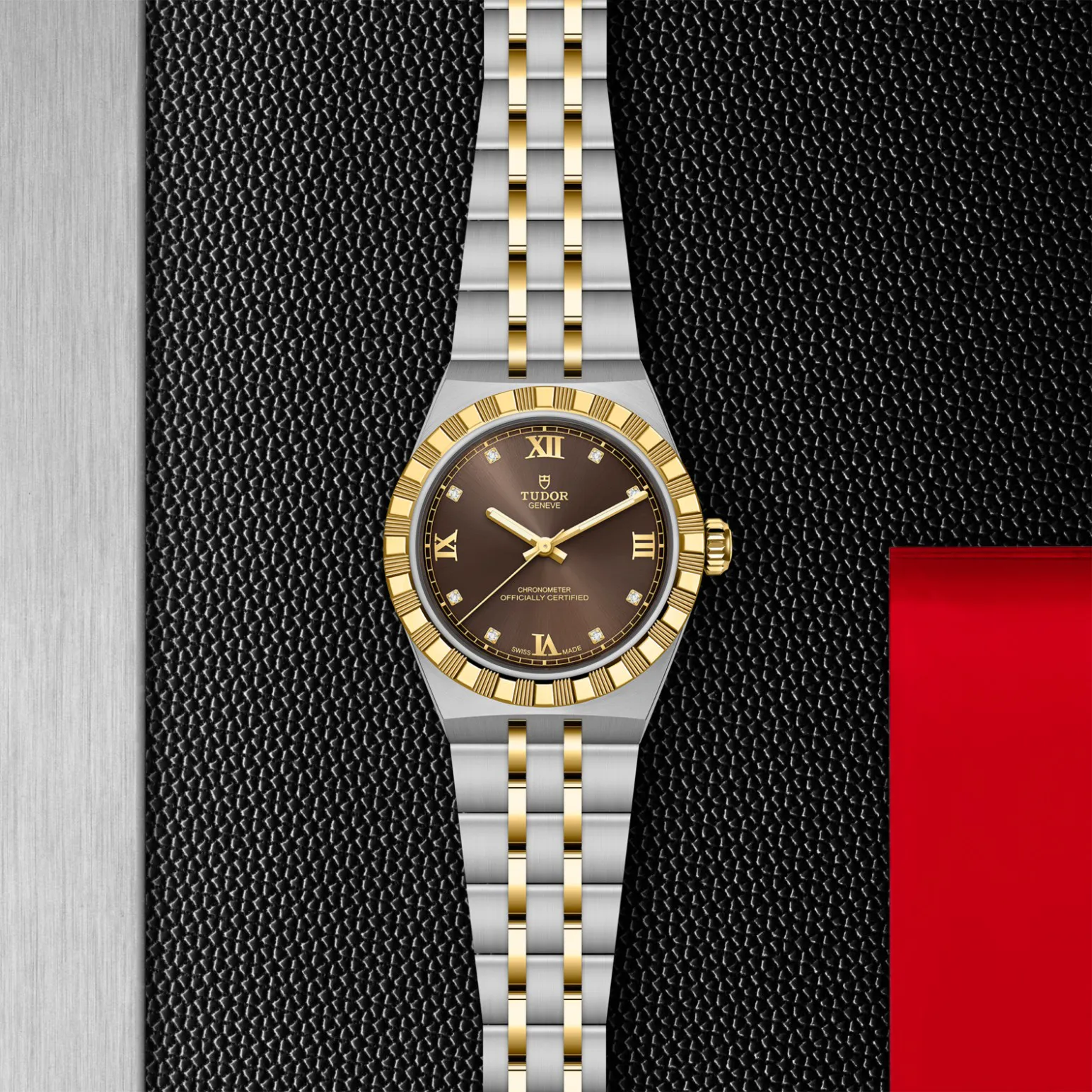 m2830a1a3-0001in_store_flat_lay | Brela Two-tone gold and steel Tudor wristwatch with a brown dial, diamond markers, and a fluted bezel on a textured black backdrop. | Brela