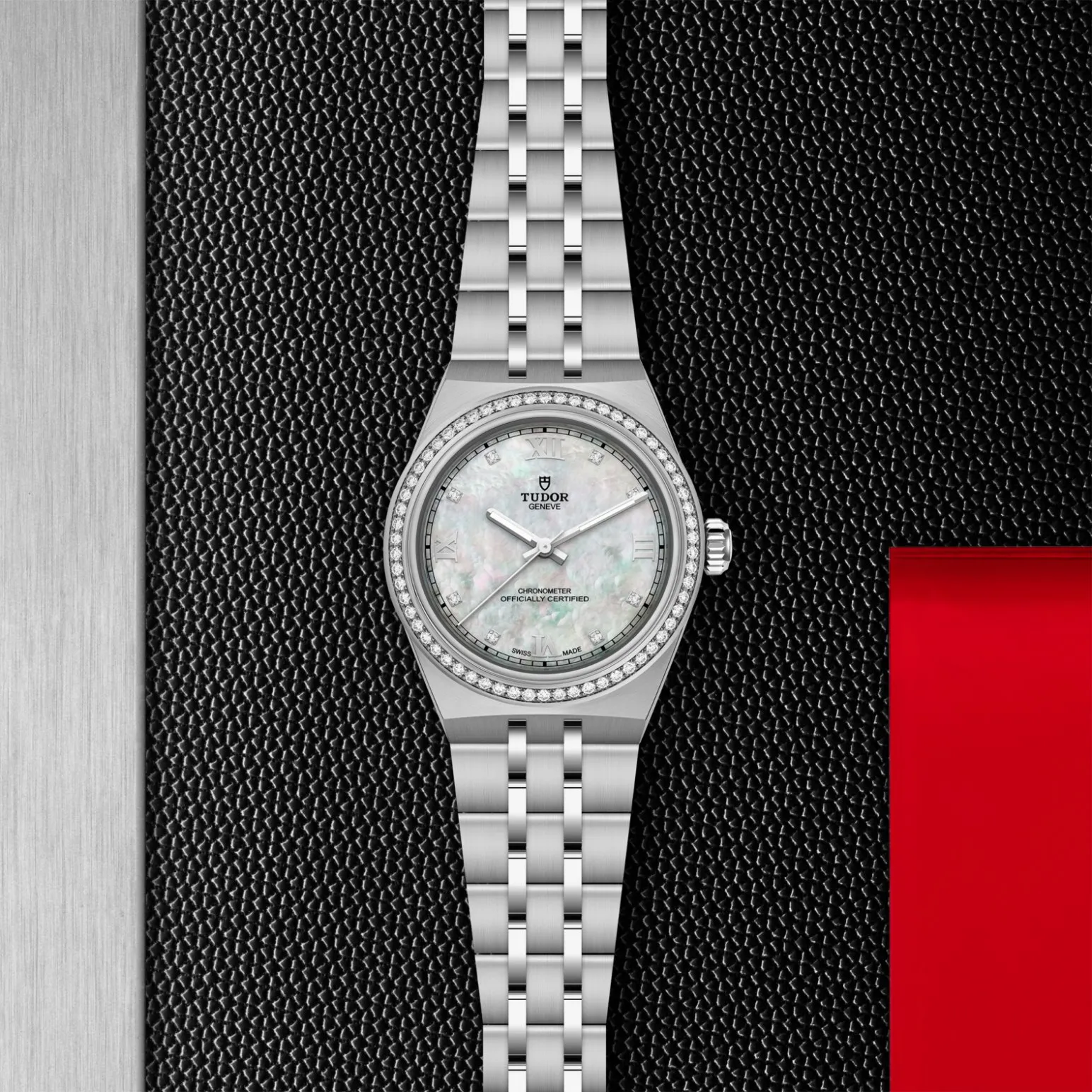 m2830a1s0-0001in_store_flat_lay | Brela Tudor Genève silver wristwatch with diamond-studded bezel and mother-of-pearl dial on black textured background | Brela