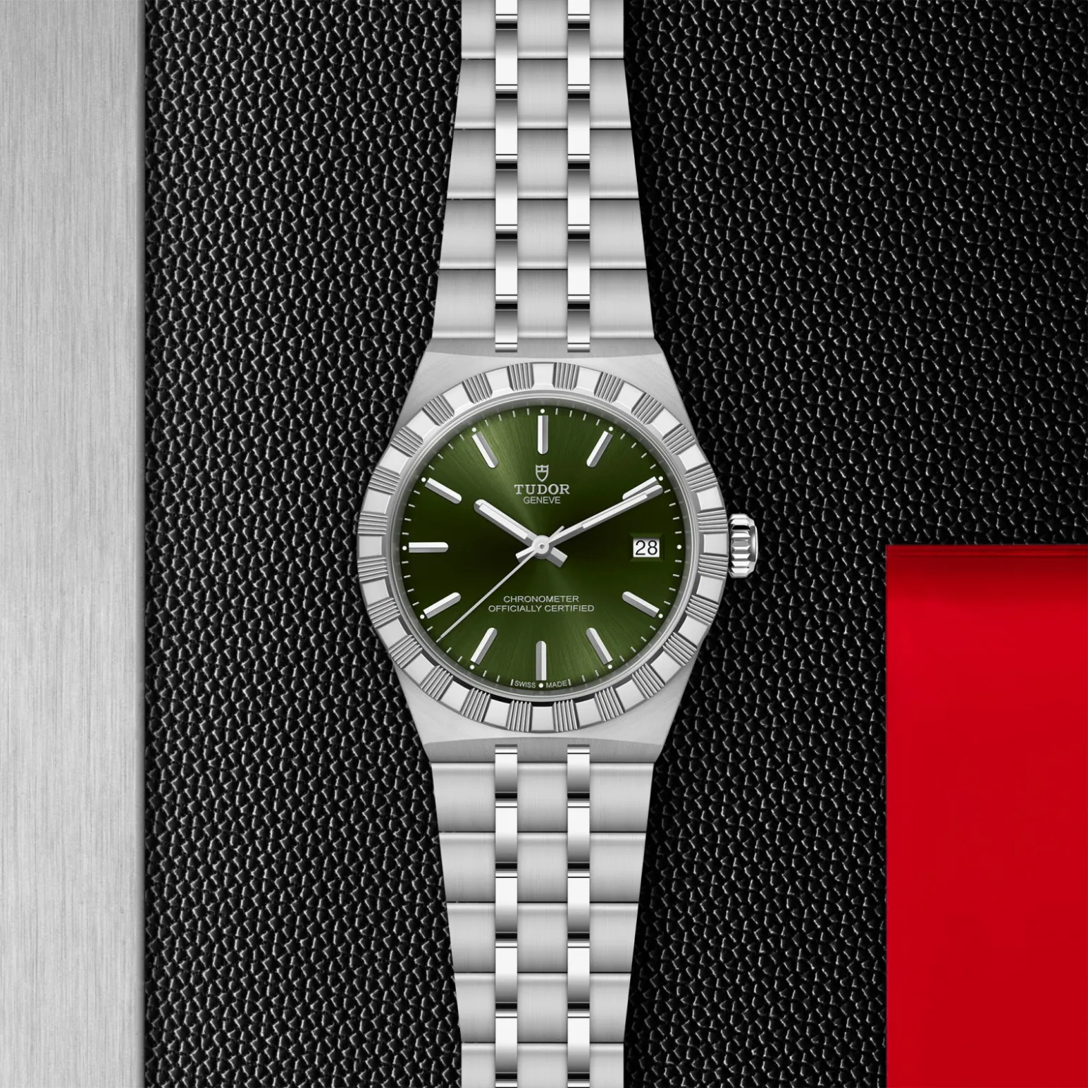 m2836c1a0-0103in_store_flat_lay | Brela Tudor wristwatch with a green dial, date window at 3 o'clock, and a stainless steel bracelet on a black textured background. | Brela