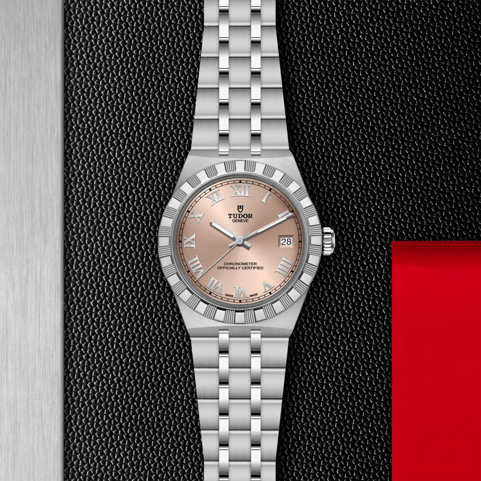 m2836c1a0-0105in_store_flat_lay | Brela Tudor stainless steel wristwatch with a rose-gold dial, Roman numerals, and date window on a textured black surface. | Brela