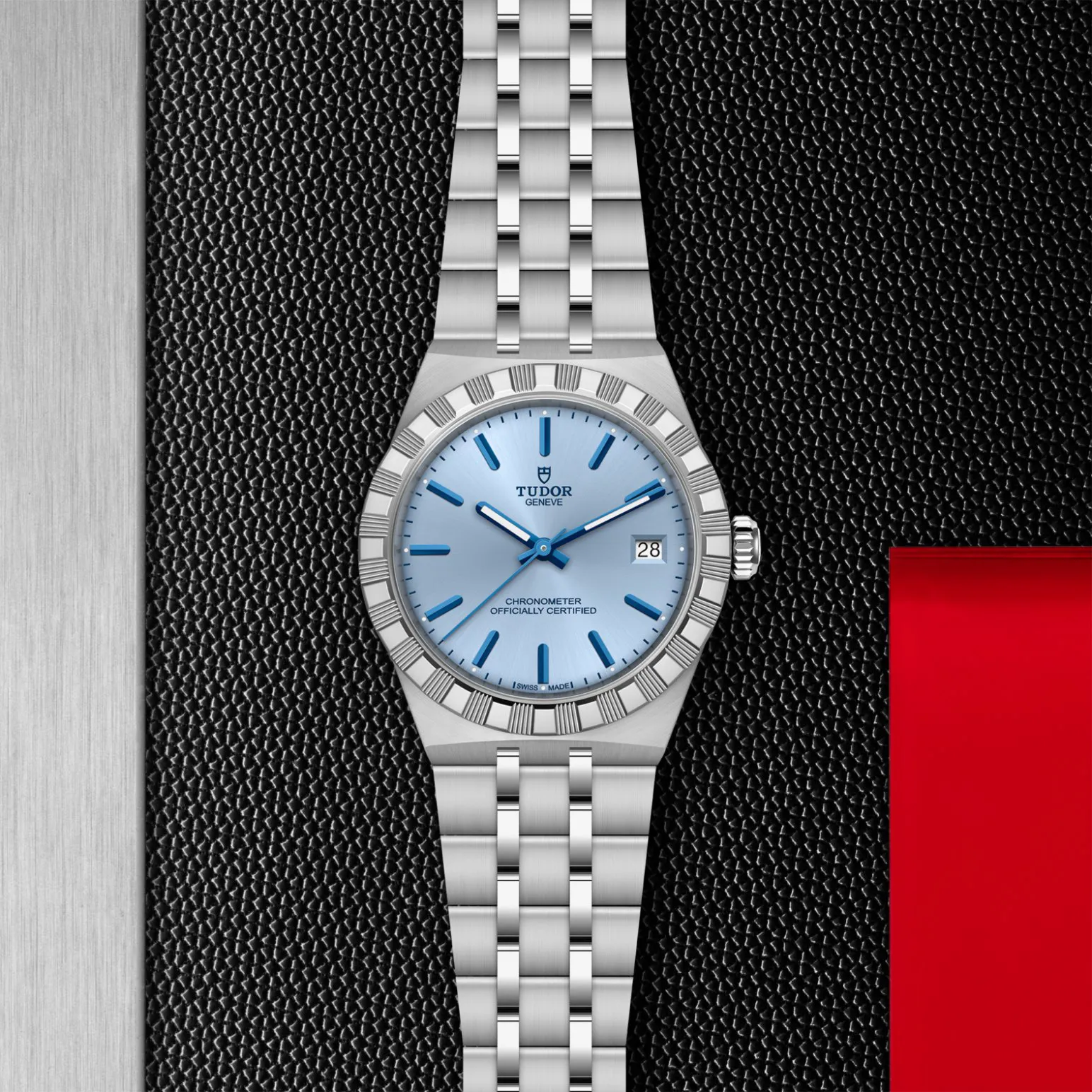 m2836c1a0-0106in_store_flat_lay | Brela Stainless steel Tudor watch with a light blue dial and date display on a textured black background. | Brela