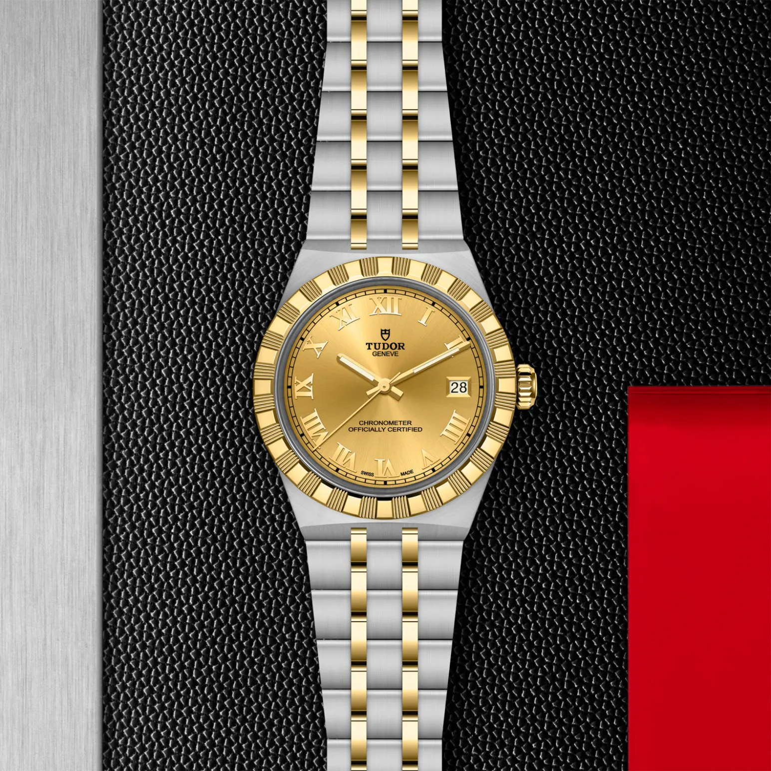 m2836c1a3-0002in_store_flat_lay | Brela Two-tone gold and stainless steel Tudor wristwatch with Roman numeral dial, date window, and a brushed band against a textured black background. | Brela