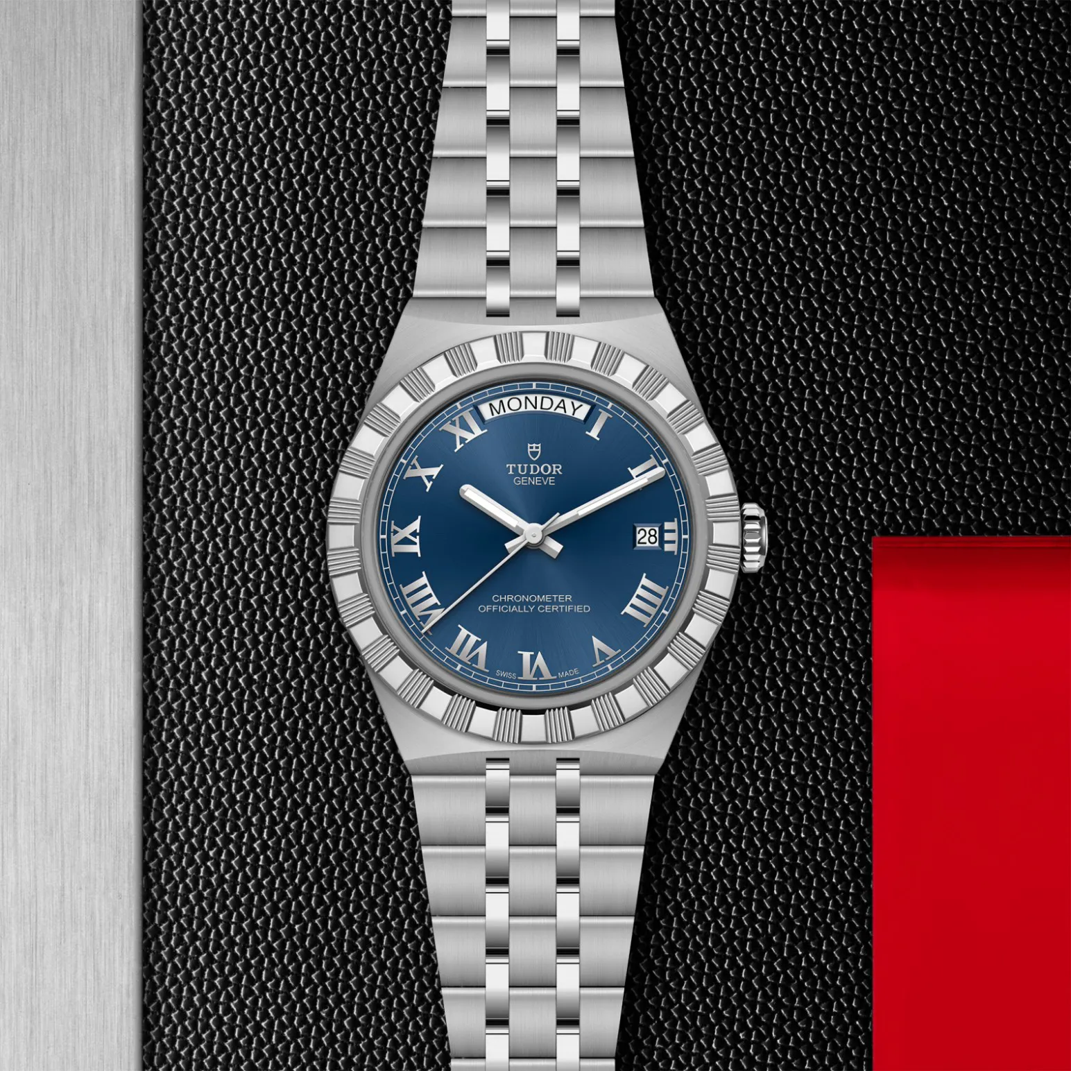 m2840d1a0-0002in_store_flat_lay | Brela Tudor stainless steel watch with blue dial, Roman numerals, date window, and metal bracelet on a textured black background | Brela