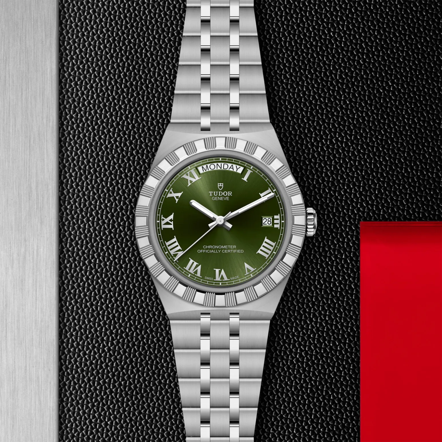 m2840d1a0-0003in_store_flat_lay | Brela Tudor watch with green dial, roman numerals, day and date window, and stainless steel bracelet on a textured black surface. | Brela