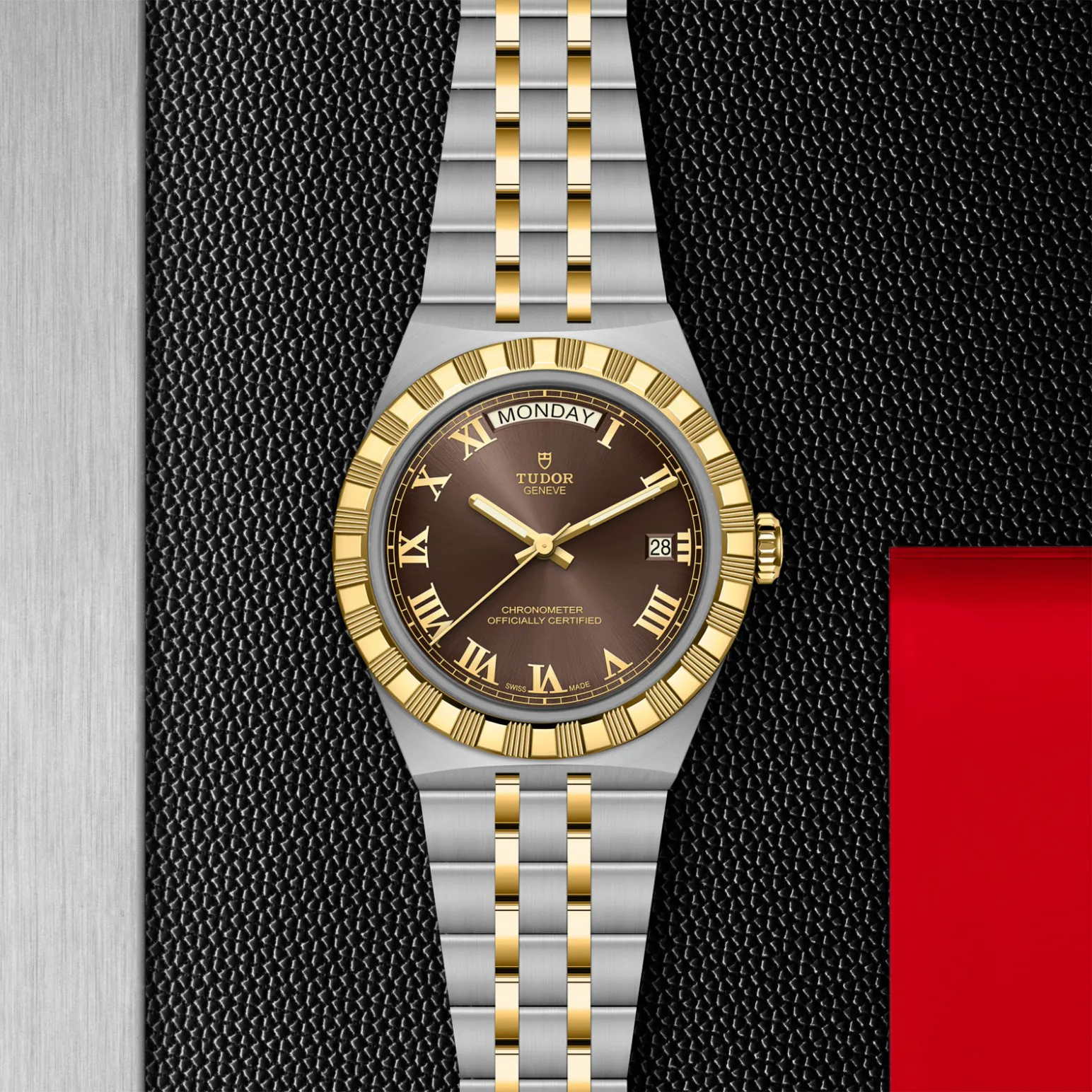 m2840d1a3-0001in_store_flat_lay | Brela Two-tone Tudor watch with a gold bezel and bracelet on a brown dial, showing a Monday day window and date, set against a black textured background. | Brela