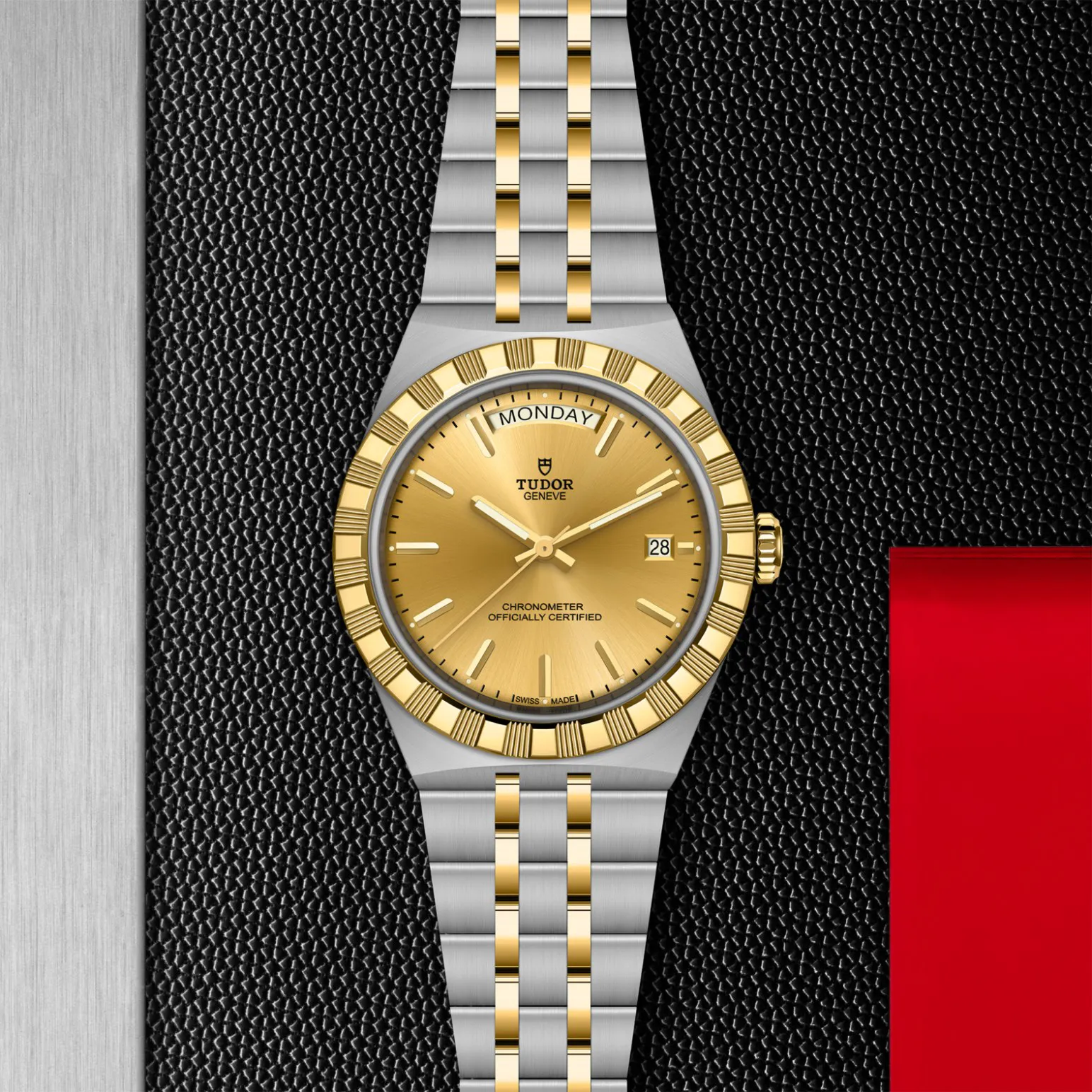 m2840d1a3-0002in_store_flat_lay | Brela Two-tone Tudor wristwatch with gold bezel and bracelet on a black textured background, displaying MONDAY and date 28 at 3 o'clock. | Brela