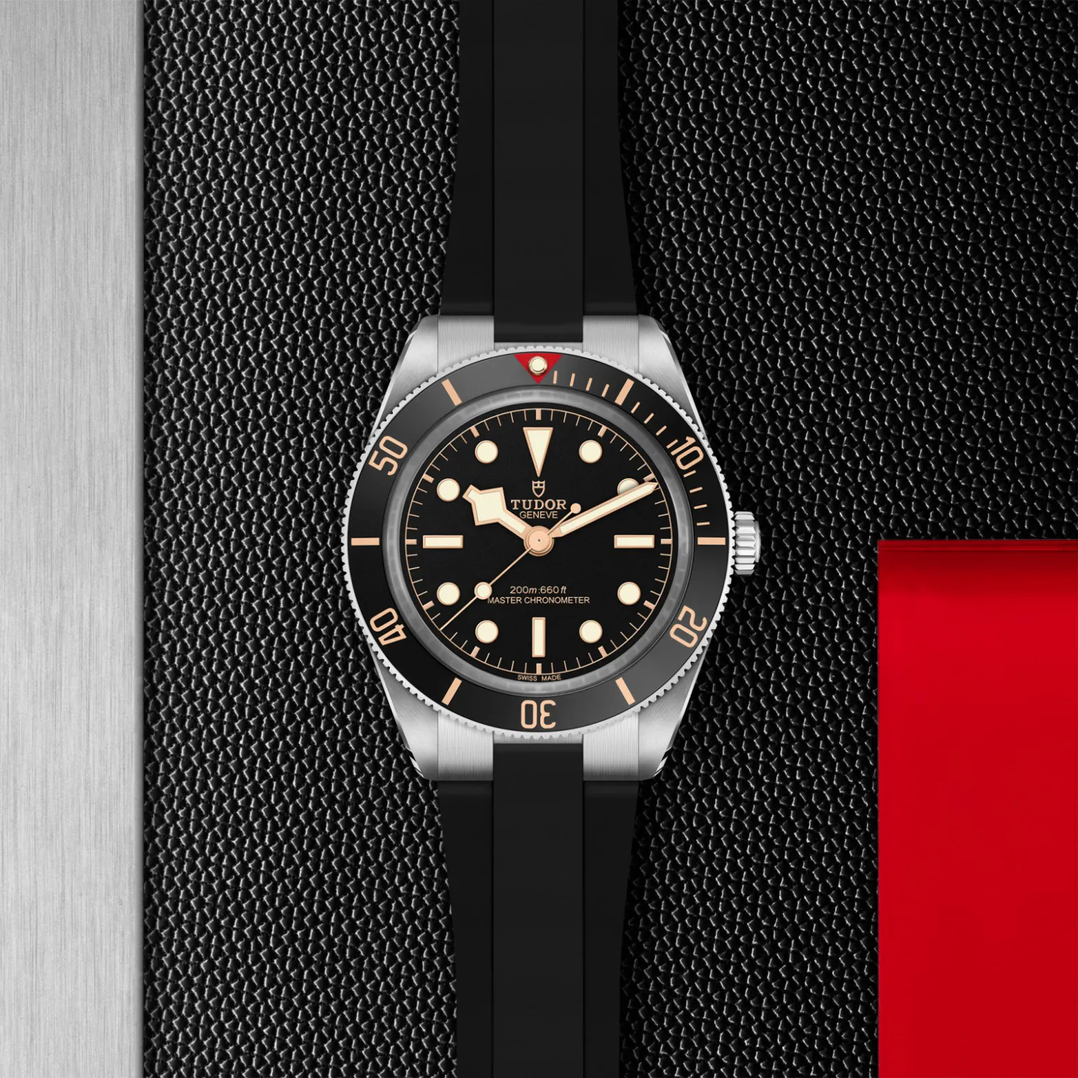 m7939a1a0nu-0003in_store_flat_lay | Brela Tudor diver's watch with black dial, gold markers, and a black rubber strap on a textured surface. | Brela