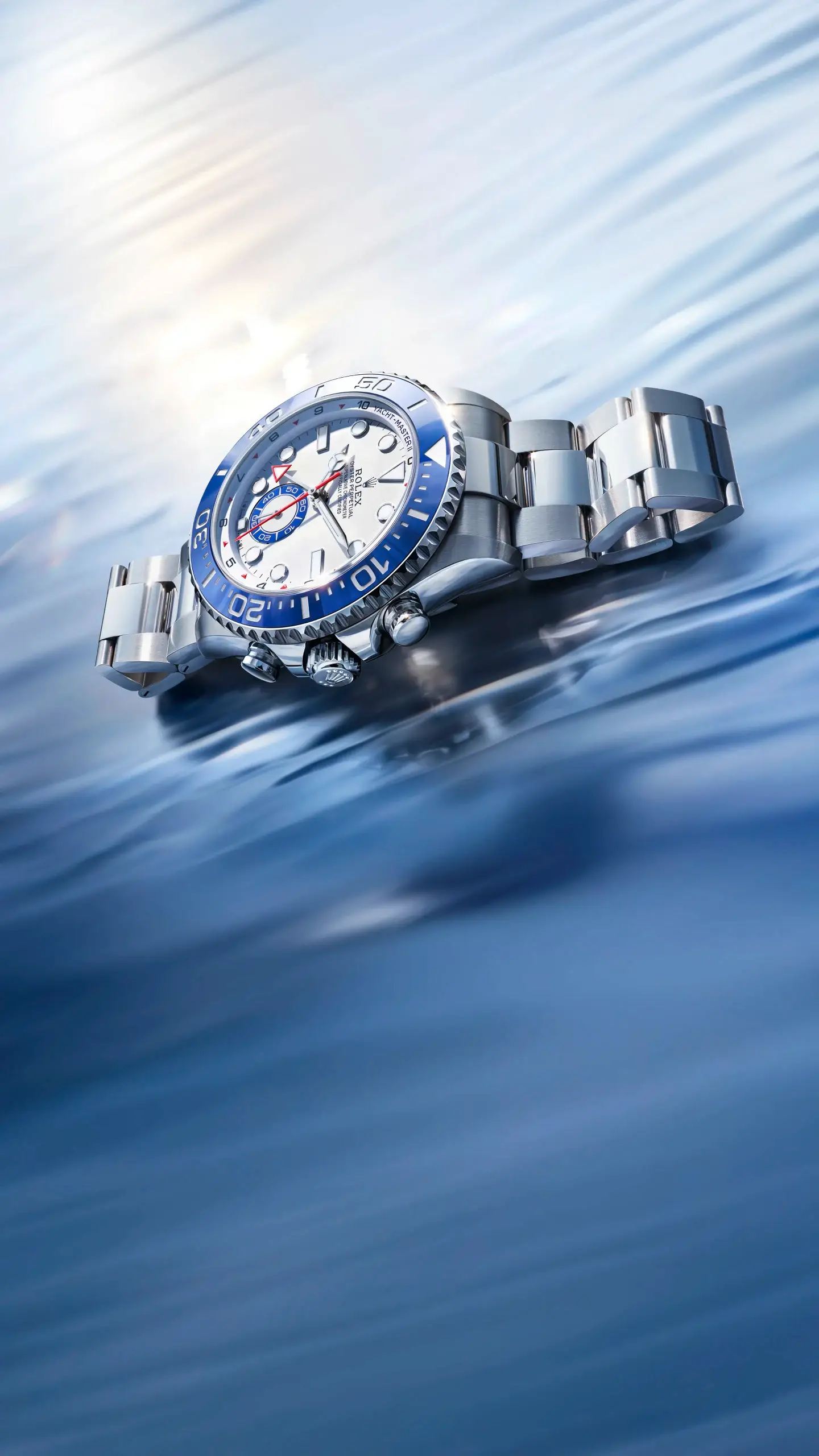 Close-up of a silver luxury dive watch with a blue bezel resting on a glossy blue water surface
